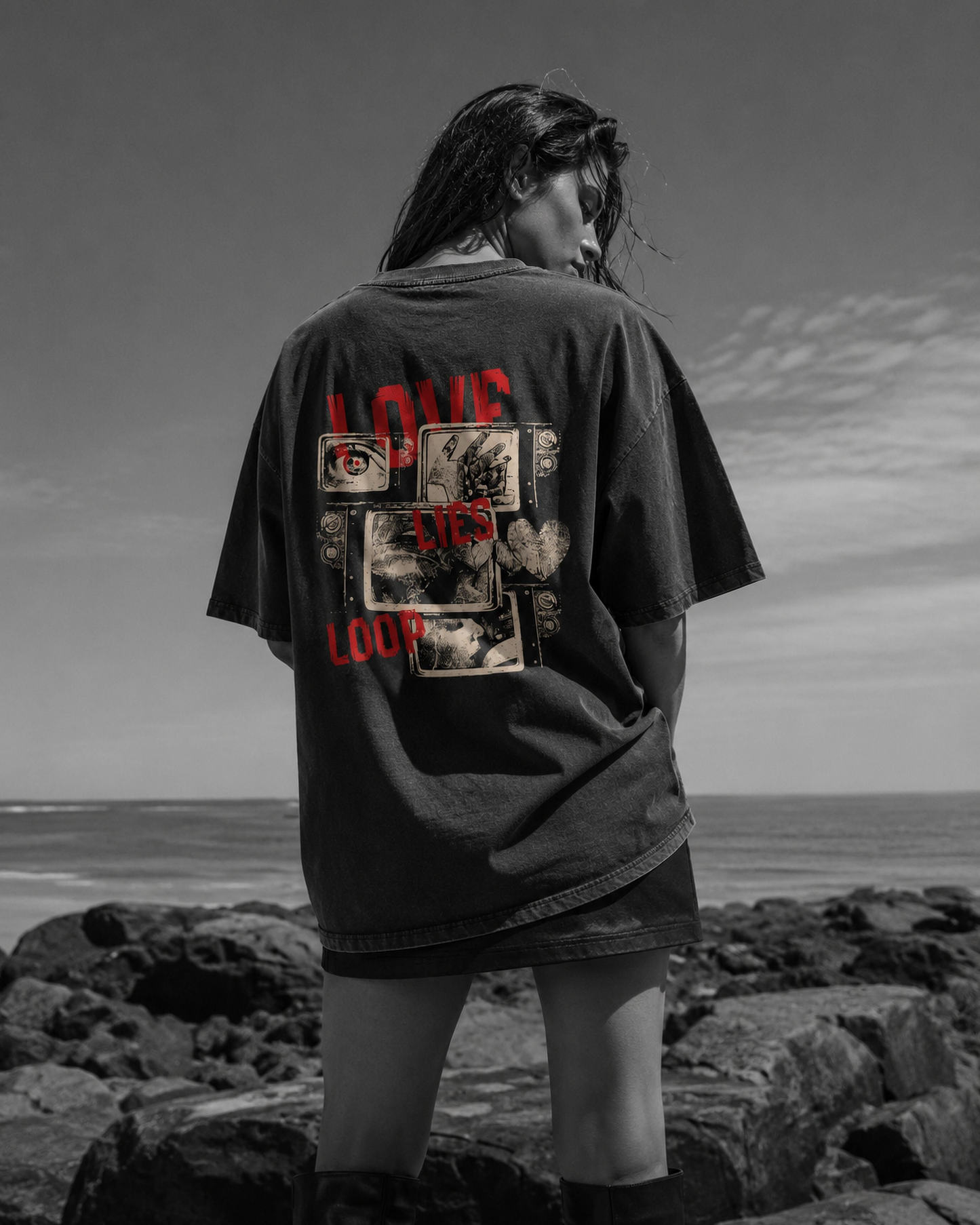 Person wearing a black t-shirt with graphic designs and text on the back, standing on rocky terrain with a scenic background.