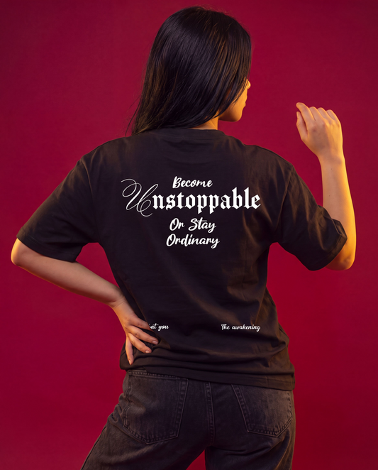 A woman shown from behind wearing a black t-shirt with white gothic-style text that reads 'Become Unstoppable Or Stay Ordinary' and smaller text 'at you' and 'The awakening' near the bottom. She is posing against a solid deep red background.