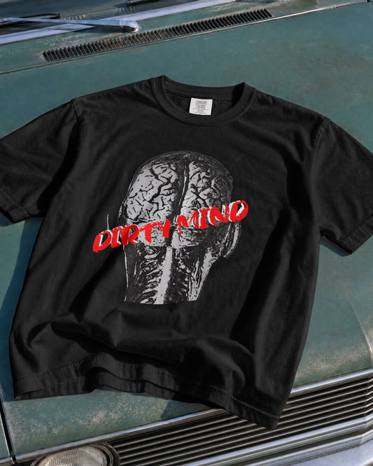 A black short-sleeve graphic t-shirt featuring a grayscale brain illustration and the words 'DIRTY MIND' in red across the chest, laid flat on the hood of a teal vintage car.
