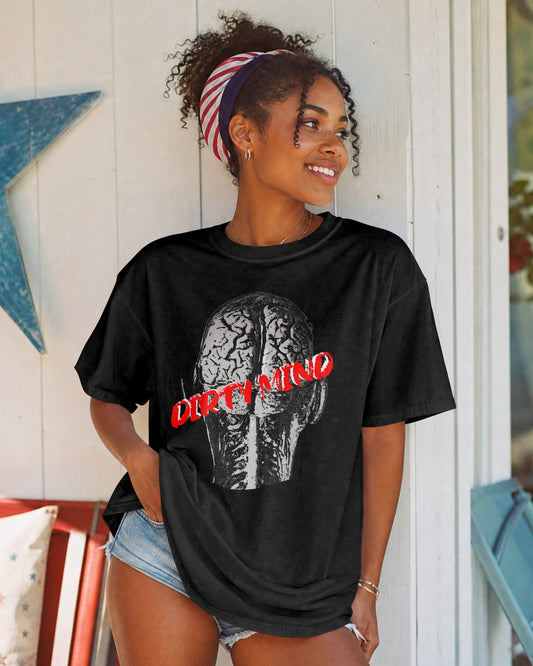 A woman wearing a black graphic t-shirt with a brain design and the text 'DIRTY MIND' in red, paired with denim shorts, posing in front of a white wooden wall decorated with a blue star.