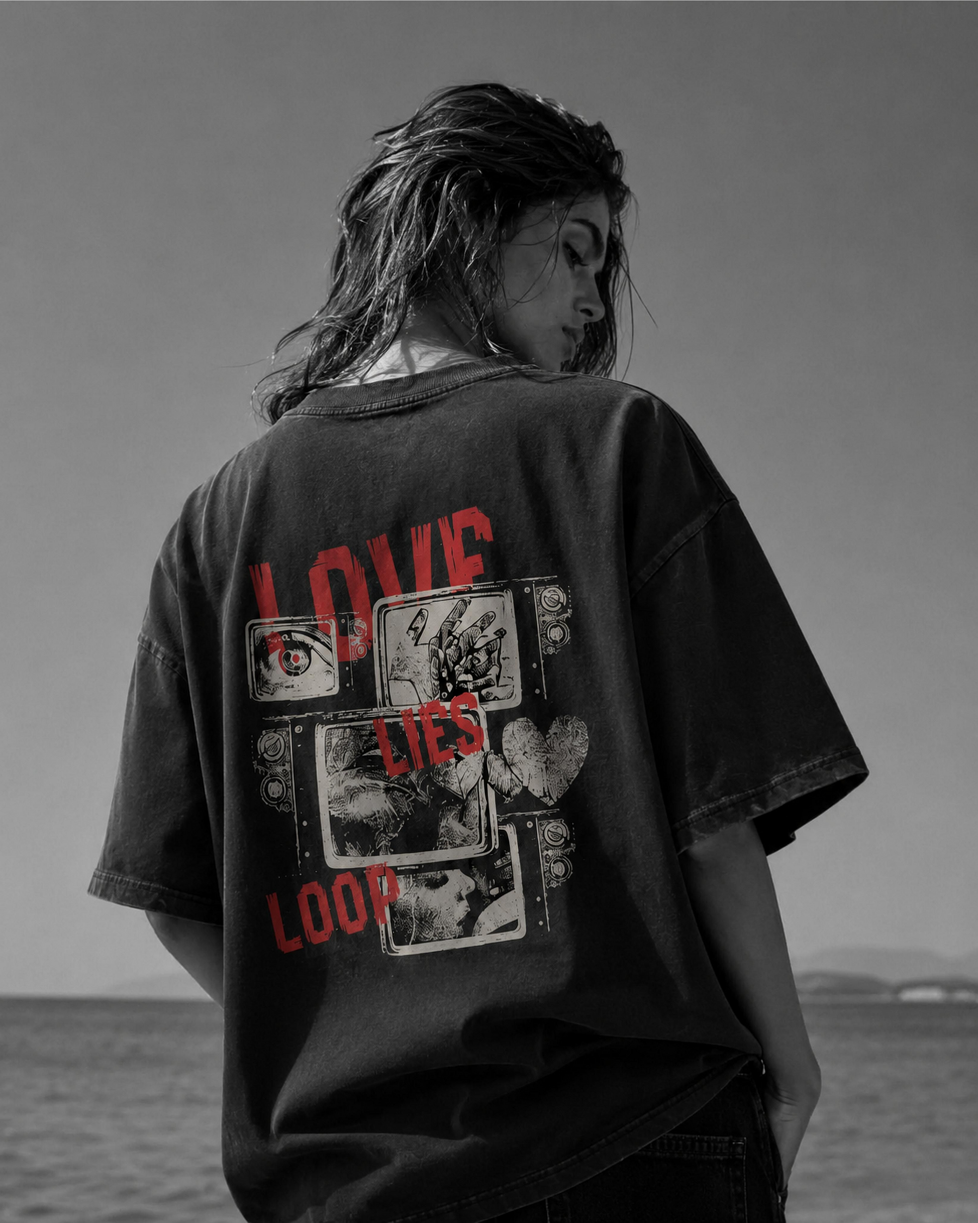 Person wearing a black t-shirt with graphic design and text, standing by a body of water.